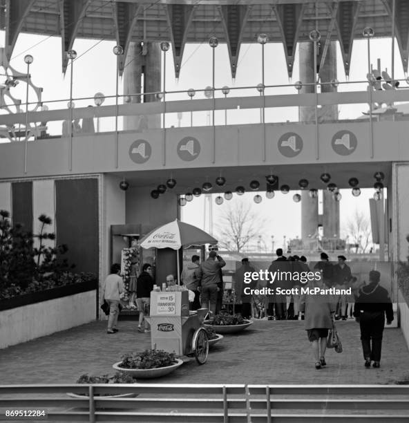 Spectators walk past a hot dog cart at the entrance to the New York State Pavilion during the 1964-65 World's Fair in Flushing Meadows Park, New...