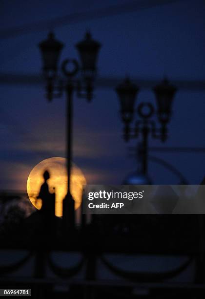 Russian girl stands on a pedestrian bridge in downtown Moscow on May 11 as a full moon is seen in the background. AFP PHOTO / Dmitry KOSTYUKOV