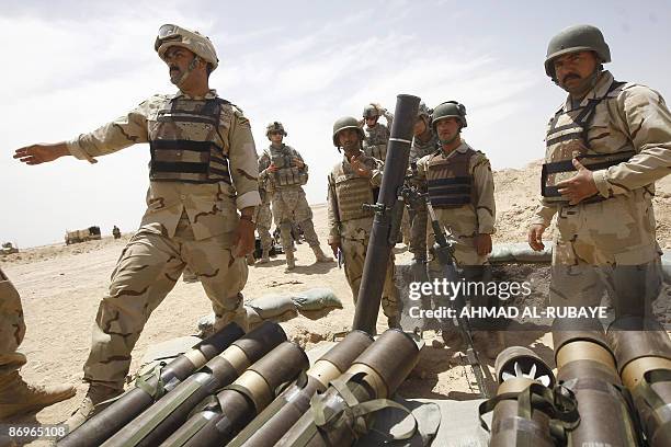 Soldier looks on as Iraqi soldiers are drilled in the use of a 120mm mortar launcher during a training operation at a desert range some 40 kms south...