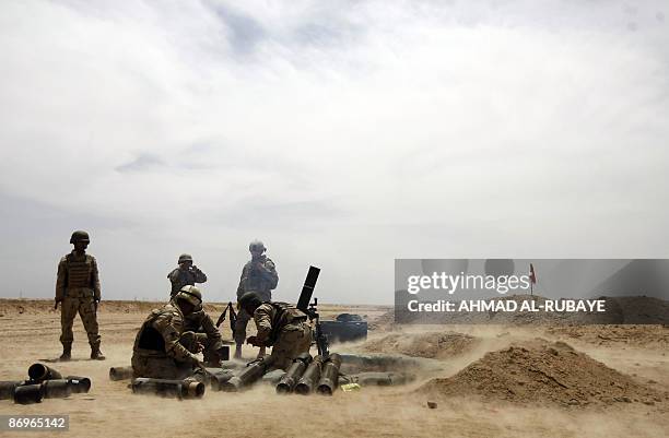 Soldiers stand by as Iraqi soldiers are drilled in the use of a 120mm mortar launcher during a training operation at a desert range some 40 kms south...