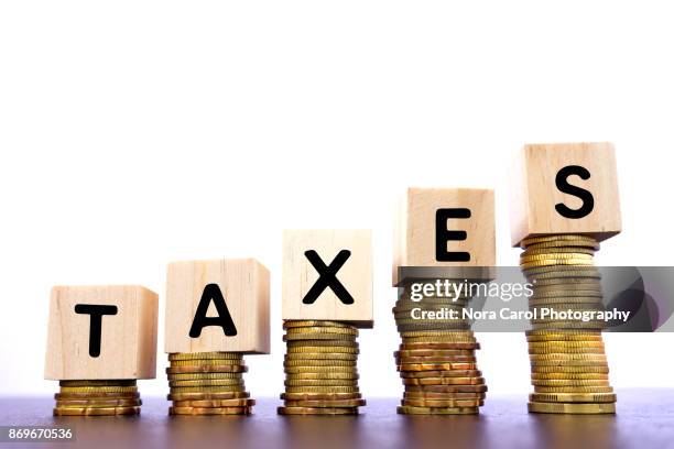 taxes word on wood block on top of coins stack - hacienda fotografías e imágenes de stock