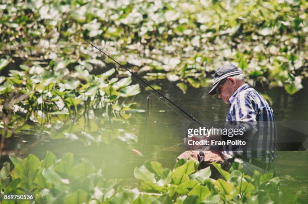 an active senior man putting bait on his fishing rod. - baldwin brothers stock pictures, royalty-free photos & images