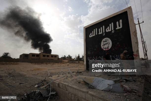 Iraqi fighters of the Hashed al-Shaabi stand next to a wall bearing the Islamic State group flag as they enter the city of al-Qaim, in Iraq's western...