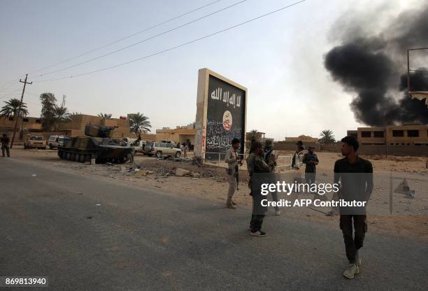 Iraqi fighters of the Hashed al-Shaabi stand next to a wall bearing the Islamic State group flag as they enter the city of al-Qaim, in Iraq's western...