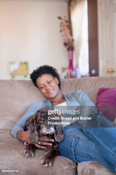 adult woman relaxing on couch hugging her cocker spaniel dog - butter curl stock-fotos und bilder