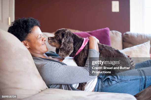 adult woman lounging on couch with her cocker spaniel dog on her lap - butter curl stock-fotos und bilder