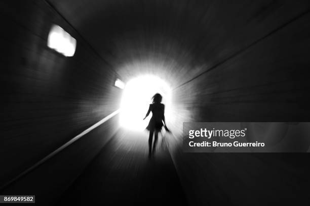 rear view silhouette of woman walking towards light at the end of tunnel - dark tunnel stock pictures, royalty-free photos & images