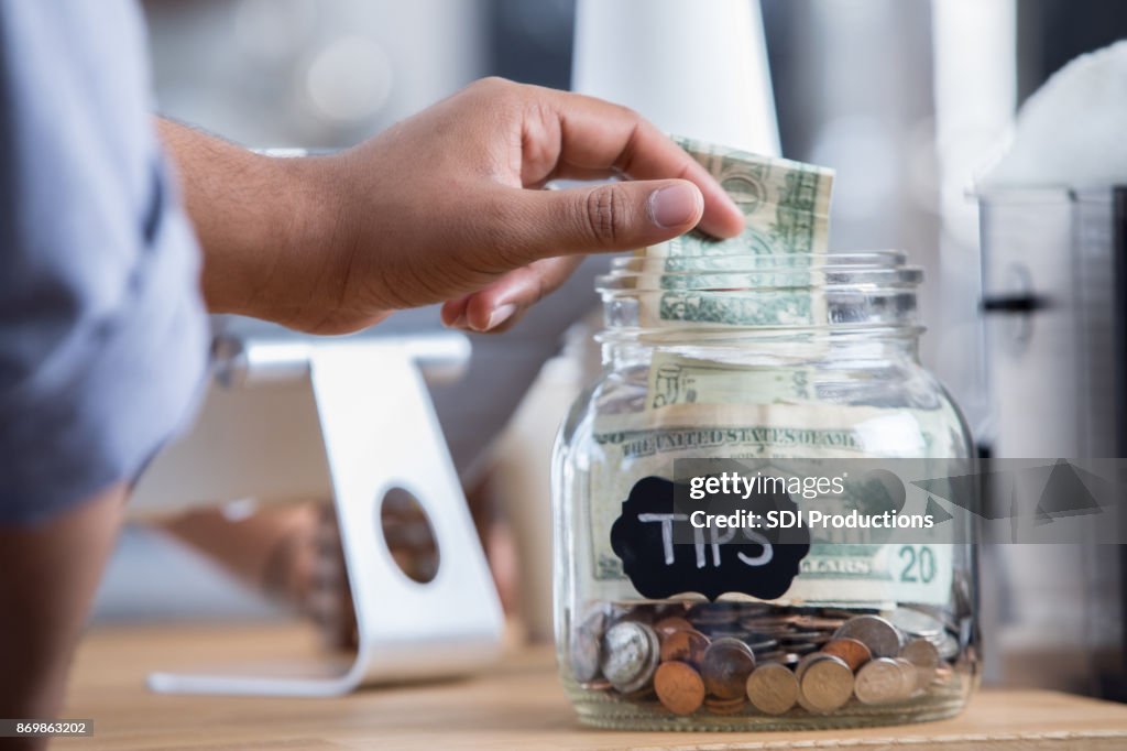 Coffeeshop klant plaatst contant geld in een tip jar