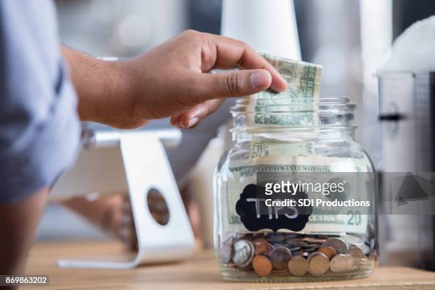 coffee shop customer places cash in a tip jar - gratuity stock pictures, royalty-free photos & images