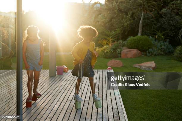 Two girls walking with can stilts on wooden terrace