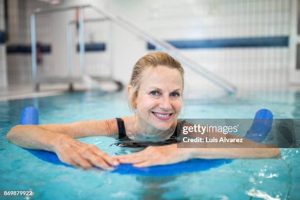 smiling mature woman swimming with noodle float in pool - mature woman swimming pool foto e immagini stock