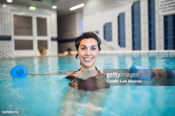 smiling mature woman exercising with dumbbells in swimming pool - hydrotherapie stockfoto's en -beelden