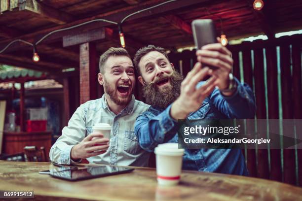 twee bebaarde vrienden drinken koffie en nemen selfie in restaurant - tache café stockfoto's en -beelden