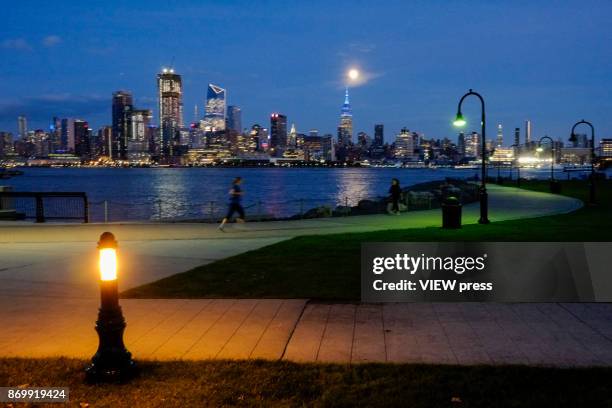 People walk along the boardwalk as the moon rise over the Empire State Building on November 2, 2017 in Hoboken, NJ.