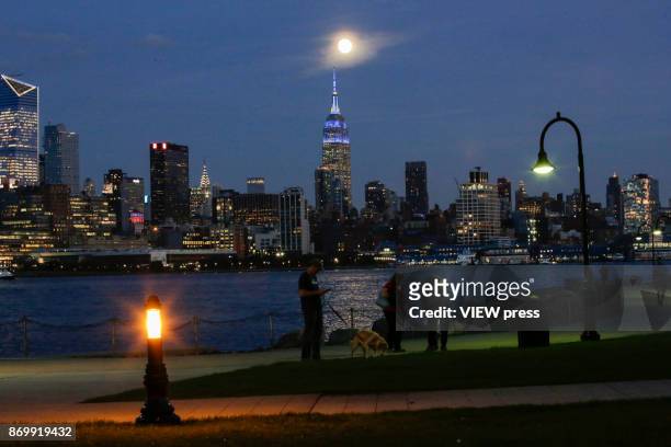 People walk along the boardwalk as the moon rise over the Empire State Building on November 2, 2017 in Hoboken, NJ.