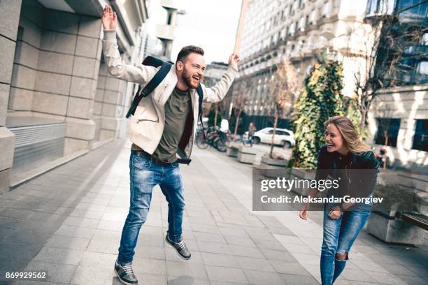 lachende teenage paar lopen en springen in de straat van de stad - studierende stockfoto's en -beelden