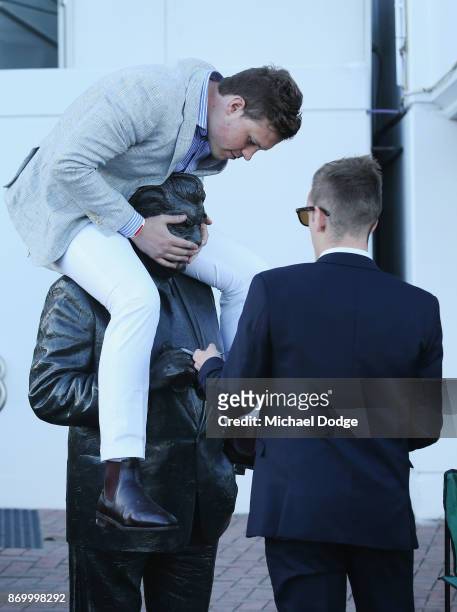 Racing fans plays around with the Bart Cummings statue after the last race on Derby Day at Flemington Racecourse on November 4, 2017 in Melbourne,...