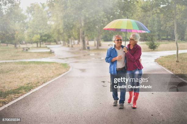 älteres paar mit einem regenbogen regenschirm - sturm der liebe stock-fotos und bilder