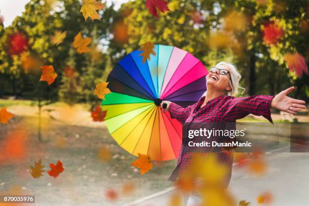 happy mature woman outdoors in autumn - multi coloured umbrella stock pictures, royalty-free photos & images