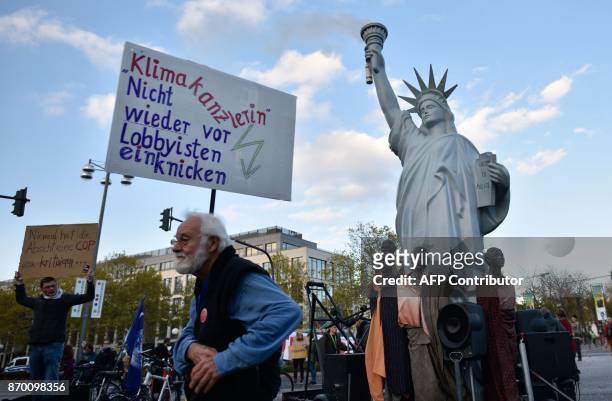 Demonstrators standing next to a mockup of the Statue of Liberty hold up a poster reading "Climate Chancellor - Don't cave in again in front of...