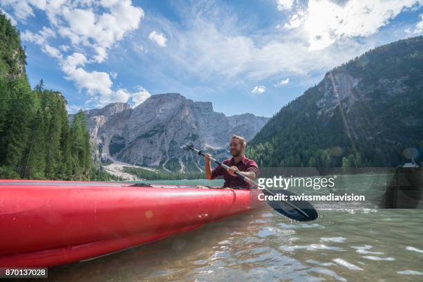 hombre joven remando la canoa roja en lago de braies, italia - bote neumático fotografías e imágenes de stock