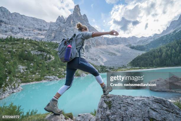 young woman jumps rock to rock near mountain lake, dolomites, italy - the next step stock pictures, royalty-free photos & images