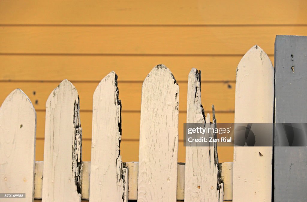 Broken white picket fence against yellow background