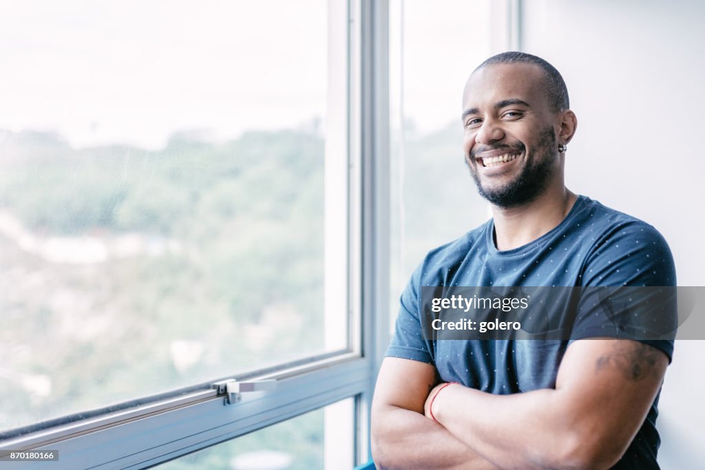 Junge lächelnde brasilianischer Geschäftsmann am Fenster im Büro