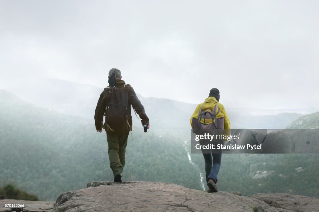 Two hikers with backpacks walking against forest and mountains