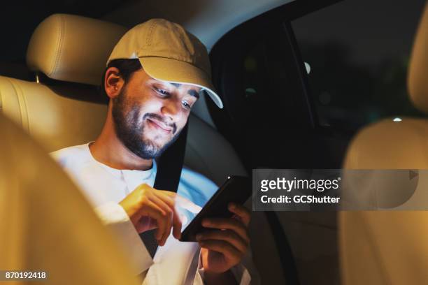 sorridendo mentre il giovane arabo legge un interessante articolo sul suo smartphone - dubai taxi foto e immagini stock