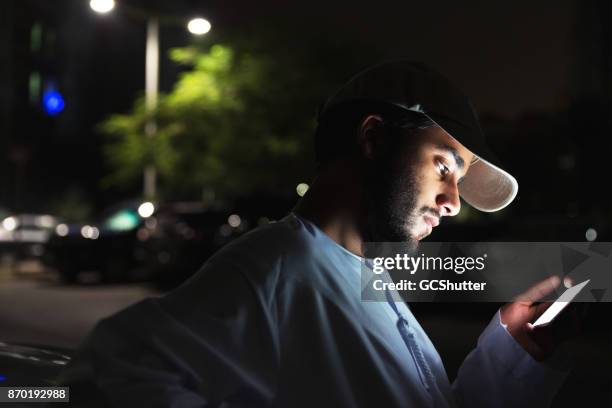 young arab streaming a show on his smart phone - dubai park stock pictures, royalty-free photos & images