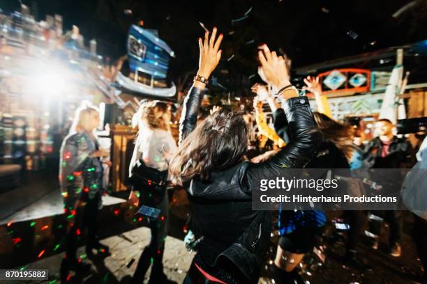 young woman throwing hands in air while dancing at open air nightclub - fiesta fotografías e imágenes de stock