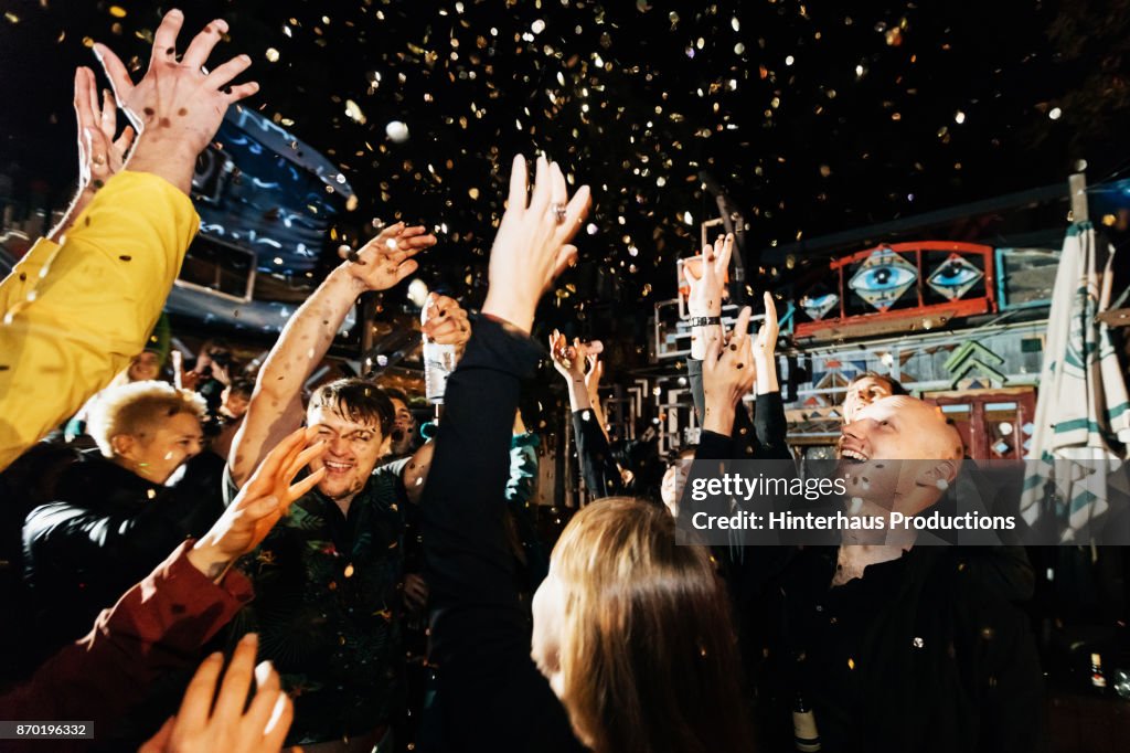 Group Of Friends Throwing Confetti In Air On Dance Floor At Open Air Nightclub