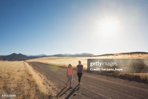 mother and daughter walking on dirt road - harpazo hope stock pictures, royalty-free photos & images