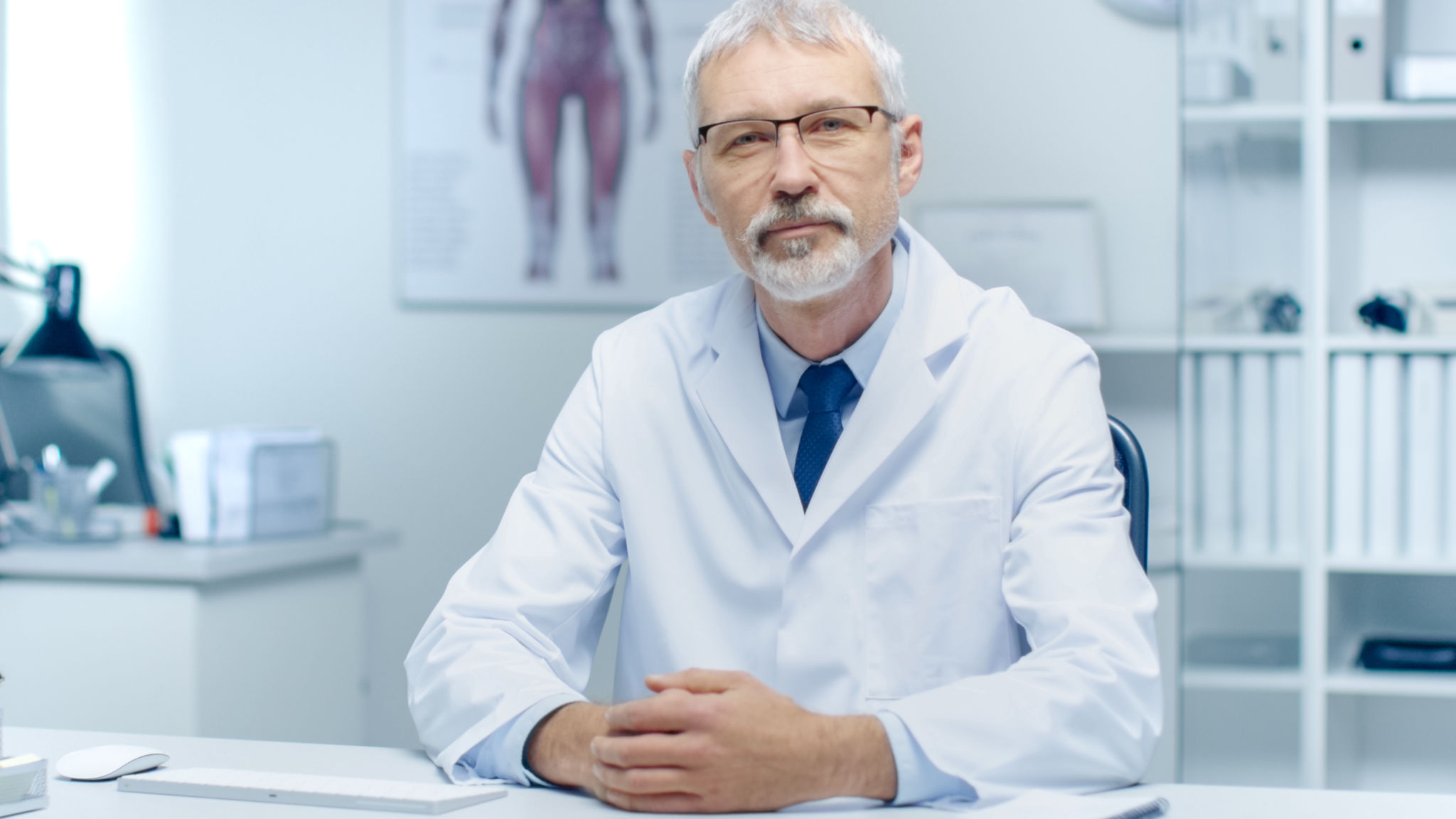 Experienced Gray Haired Senior Medical Practitioner Smiling and Looking Into Camera. Portrait Shot in Modern and Light Office. Experienced Gray Haired Senior Medical Practitioner Smiling and Looking Into Camera. Portrait Shot in Modern and Light Office.