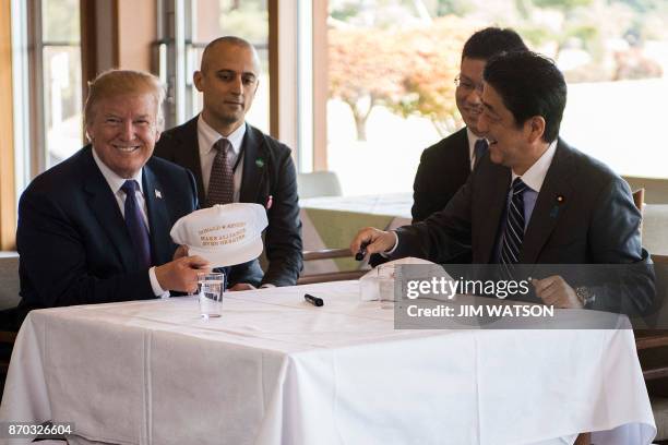 President Donald Trump holds up a hat as he speaks with Japan's Prime Minister Shinzo Abe during a luncheon at the Kasumigaseki Country Club Golf...