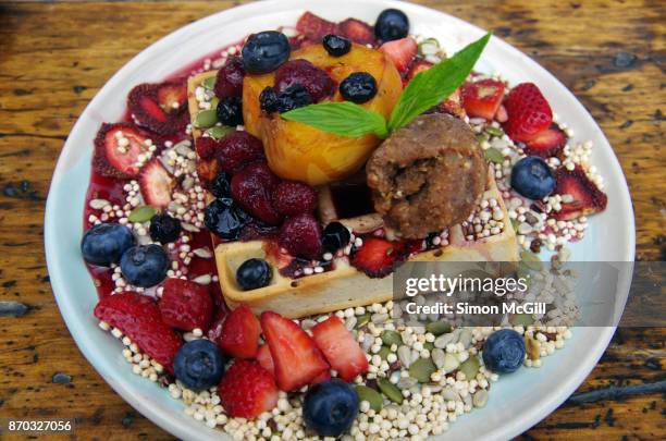 vegan banana and nut waffle with banana cashew cream, vegan nutella, mixed fresh and dehydrated berries, roasted peach, mixed seeds and puffed millet and maple syrup - coulis stock pictures, royalty-free photos & images