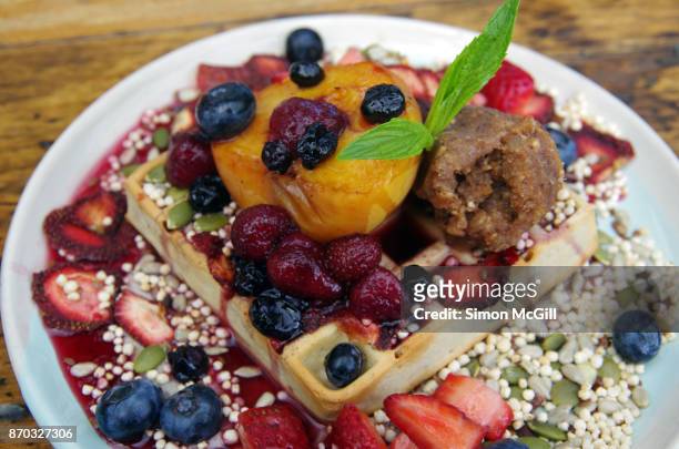 vegan banana and nut waffle with banana cashew cream, vegan nutella, mixed fresh and dehydrated berries, roasted peach, mixed seeds and puffed millet and maple syrup - coulis stock pictures, royalty-free photos & images