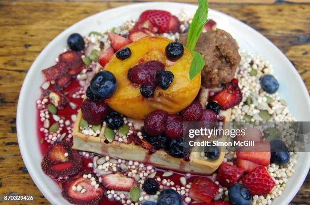 vegan banana and nut waffle with banana cashew cream, vegan nutella, mixed fresh and dehydrated berries, roasted peach, mixed seeds and puffed millet and maple syrup - coulis stock pictures, royalty-free photos & images