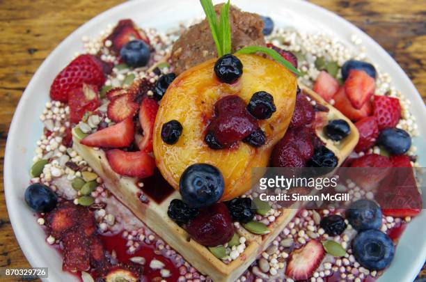vegan banana and nut waffle with banana cashew cream, vegan nutella, mixed fresh and dehydrated berries, roasted peach, mixed seeds and puffed millet and maple syrup - coulis stock pictures, royalty-free photos & images