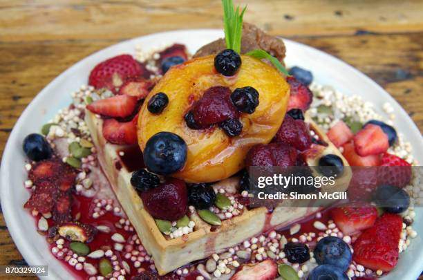 vegan banana and nut waffle with banana cashew cream, vegan nutella, mixed fresh and dehydrated berries, roasted peach, mixed seeds and puffed millet and maple syrup - coulis stock pictures, royalty-free photos & images