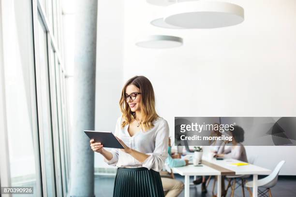 young businesswoman working in modern office on a digital tablet - digital tablet stock pictures, royalty-free photos & images