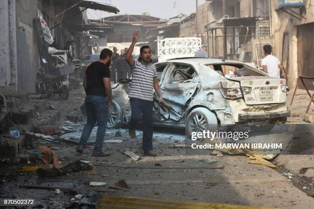 Graphic content / Iraqi men stand next to the remains of a body as they inspect the scene of a twin suicide attack at shopping area in Iraq's...