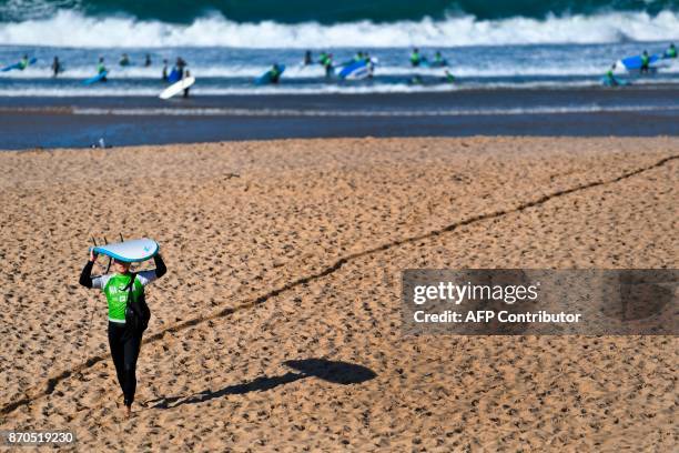 Man carries a surfboard after a surf lesson at Foz do Lizandro beach in Ericeira on November 5, 2017 during a 2017 Web Summit surf event for...