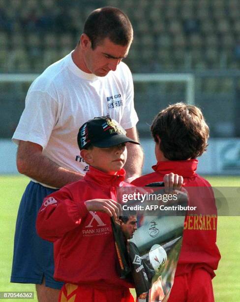 Le footballeur Eric Cantona, qui vient d'annoncer sa retraite, dédicace des posters pour des jeunes supporters, le 25 mai sur la pelouse du stade...