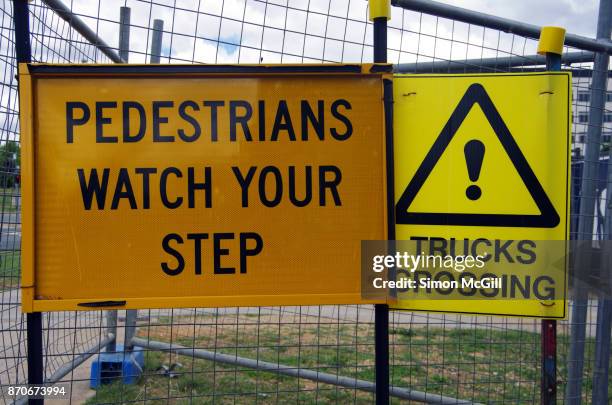 pedestrians watch your step and trucks crossing signs next to a construction site beside a road - trip hazard stock pictures, royalty-free photos & images
