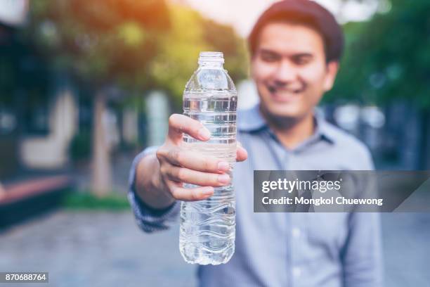 young asian handsome business man show bottle of water in a park - suit hand stock-fotos und bilder