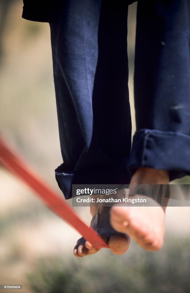 Close up of a man's bare feet balancing on a tight rope or slackline in the California desert.
