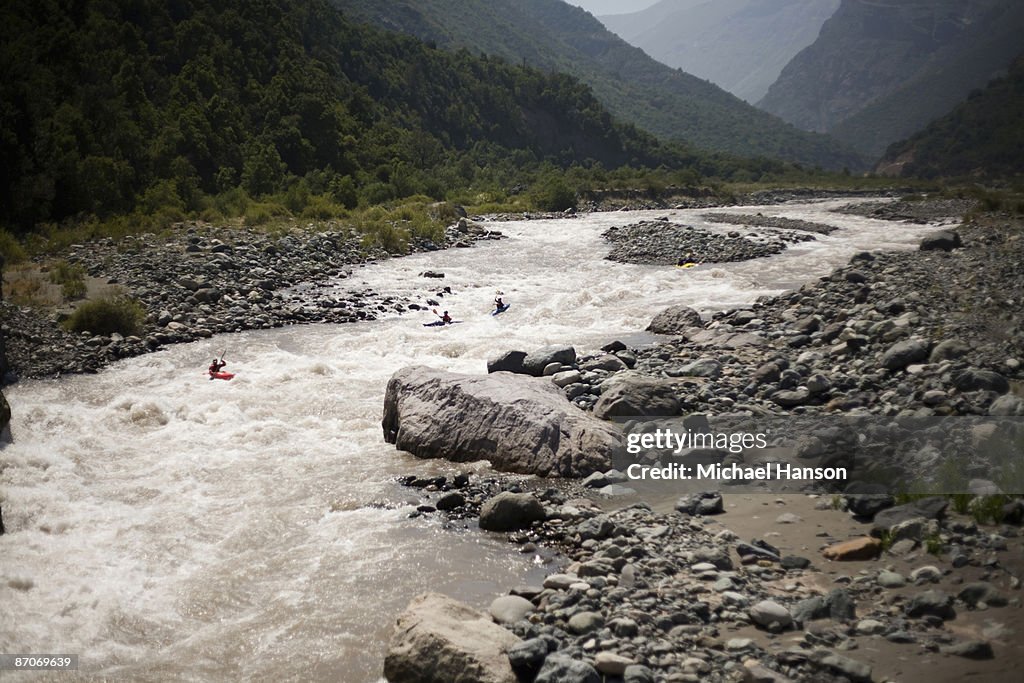 Four kayakers paddle through whitewater on a river in Chile.