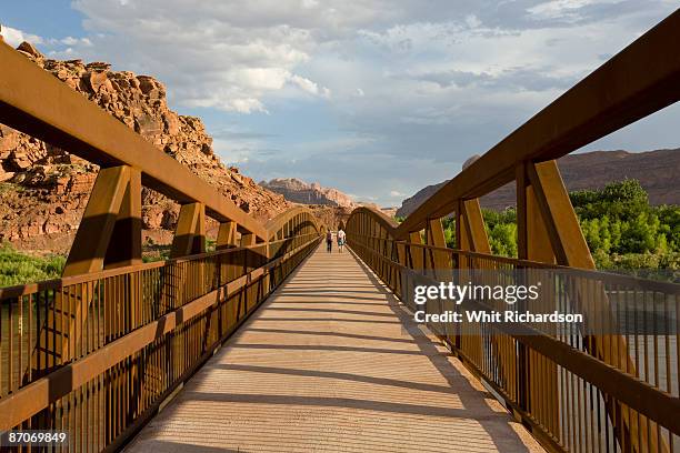 two people in distance walking across bridge in moab, utah. - コロラド川 ストックフォトと画像